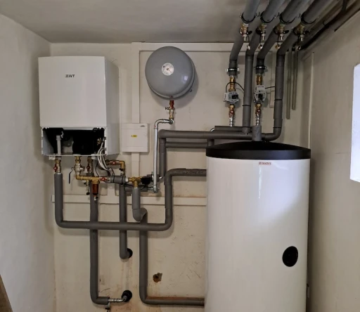 Bílý plynový kotel a ohřívač vody v technické místnosti s připojenými trubkami a měřidly.