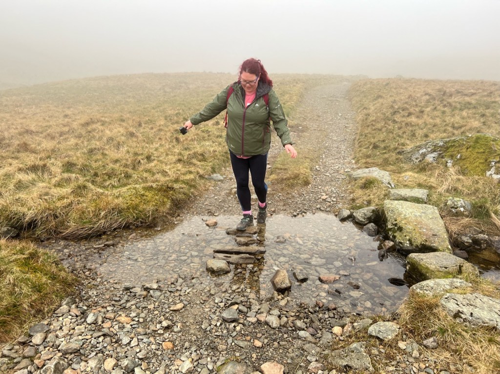 April crossing a big puddle in the path by stepping on some large stones in the middle. Balancing with her arms out.