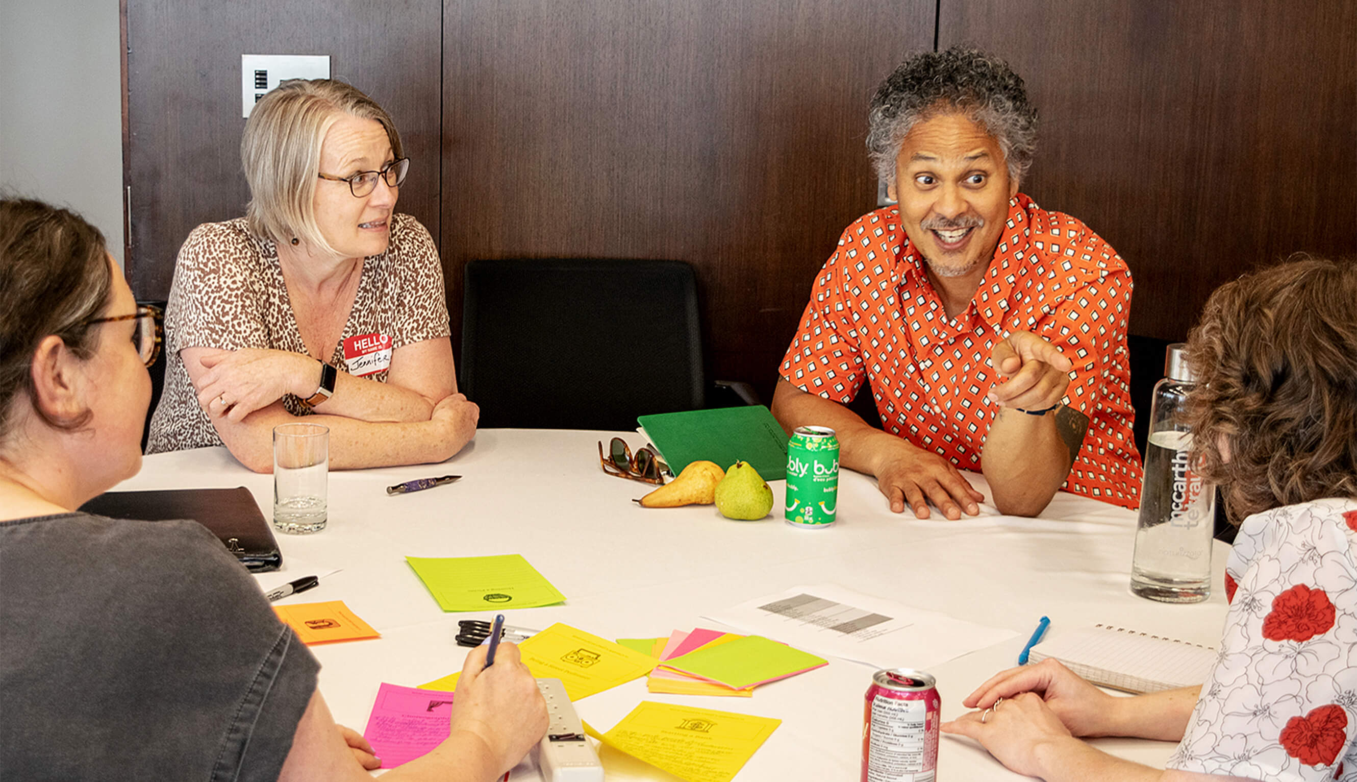 Four people sitting around a table filled with notes. One person actively pointing and smiling.