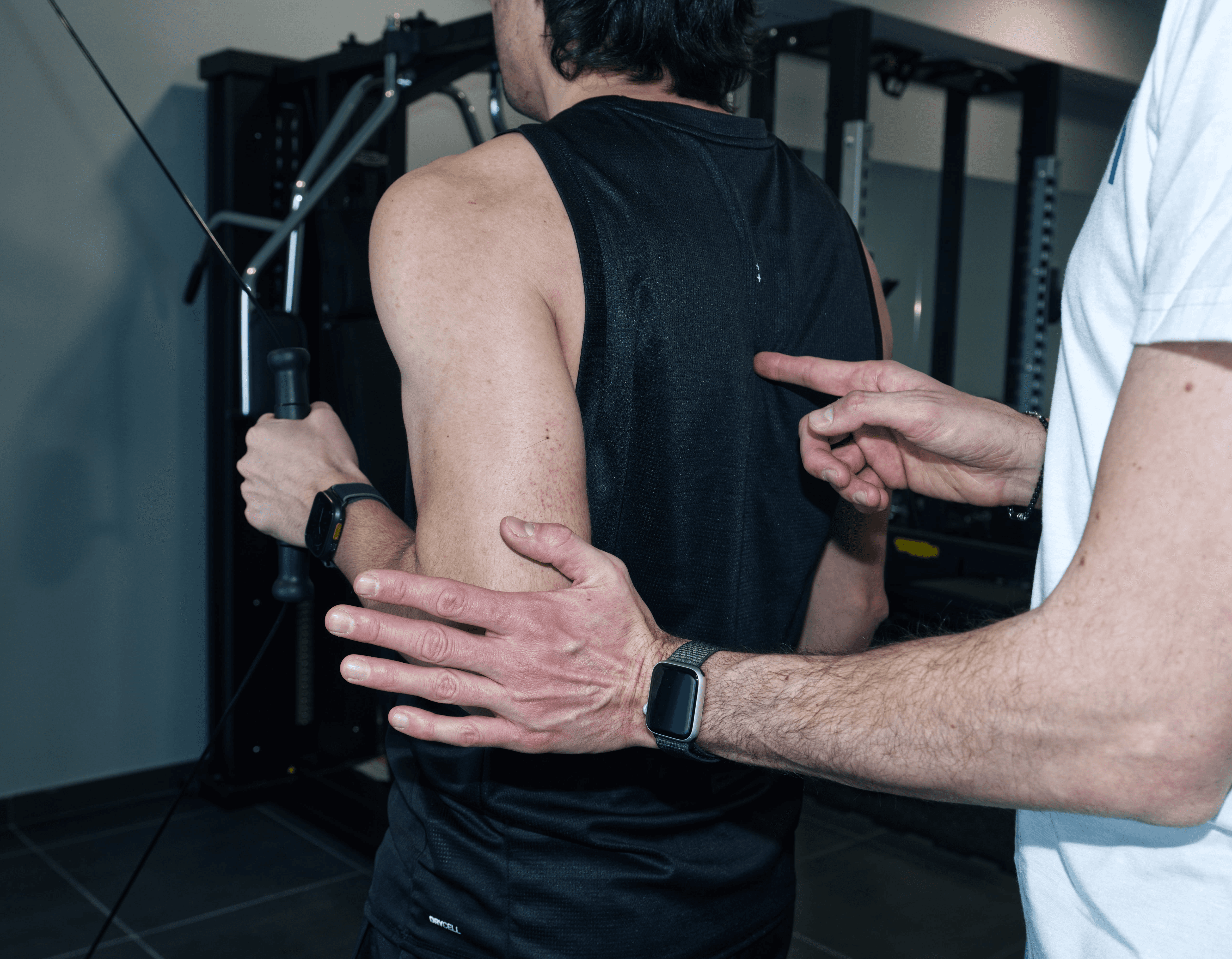 A person sits at a cluttered desk in a dimly lit room, focused on two monitors displaying aerial maps. The walls are covered with various images and notes.