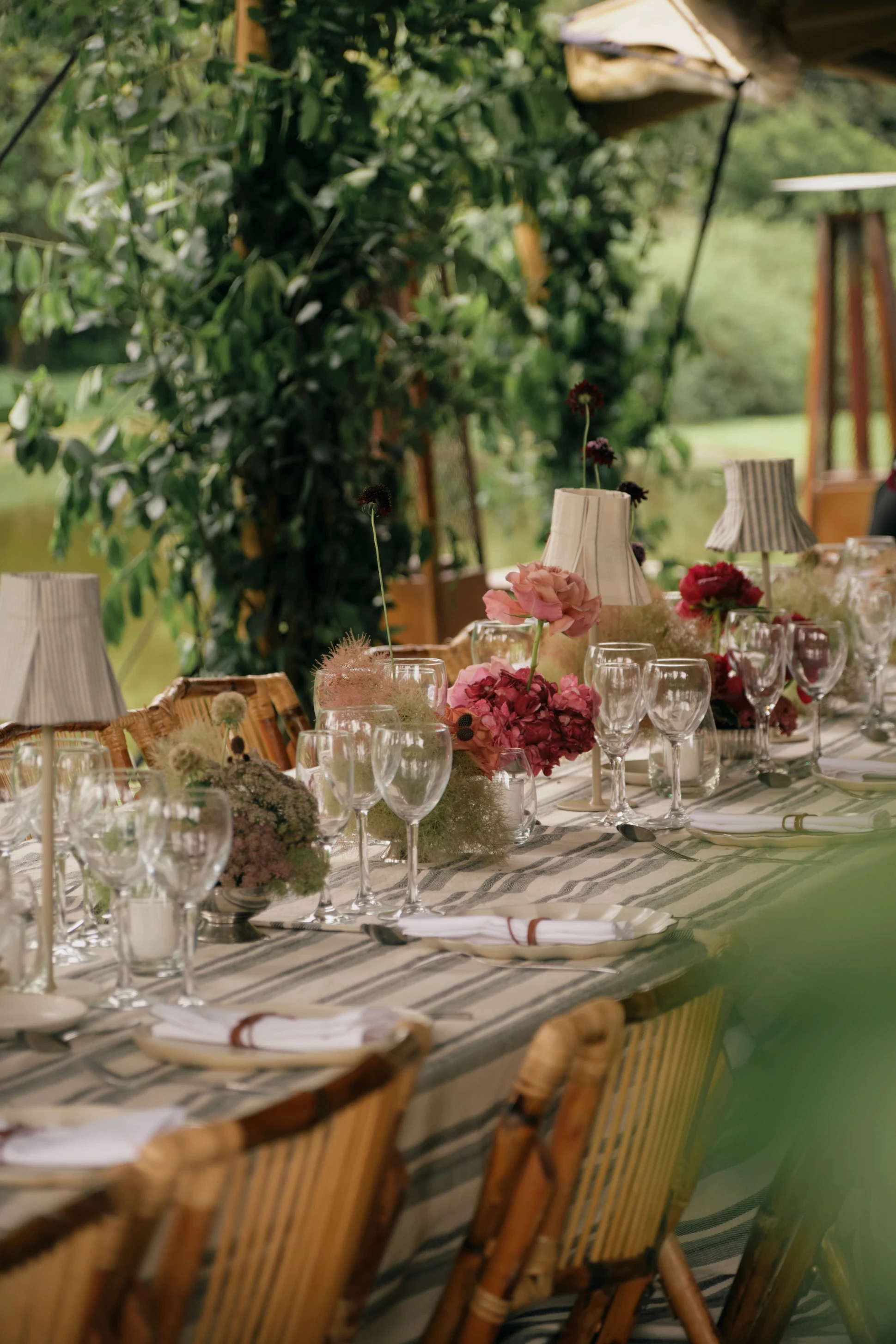 Perspectiva de mesa de banquete al aire libre con hiedra colgante y arreglos florales en tonos fucsia y rosa.