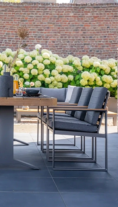 Stylish outdoor dining area featuring a wooden table, sleek chairs, and a backdrop of blooming hydrangeas against a brick wall.