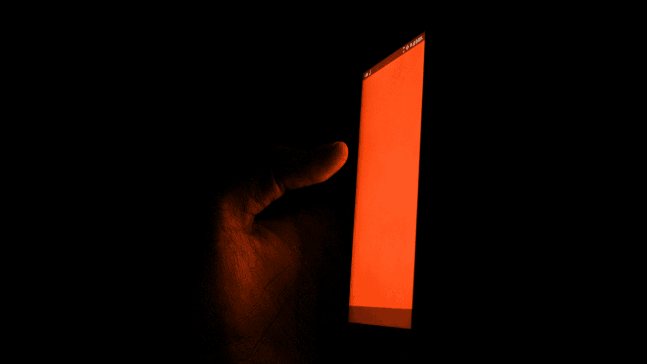 Hand holding a glowing orange smartphone screen in the dark.