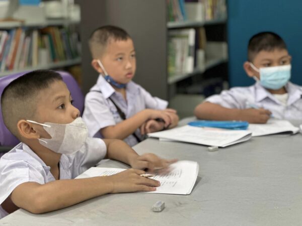 man in blue t-shirt and white floral skirt holding black smartphone while sitting on sidewalk