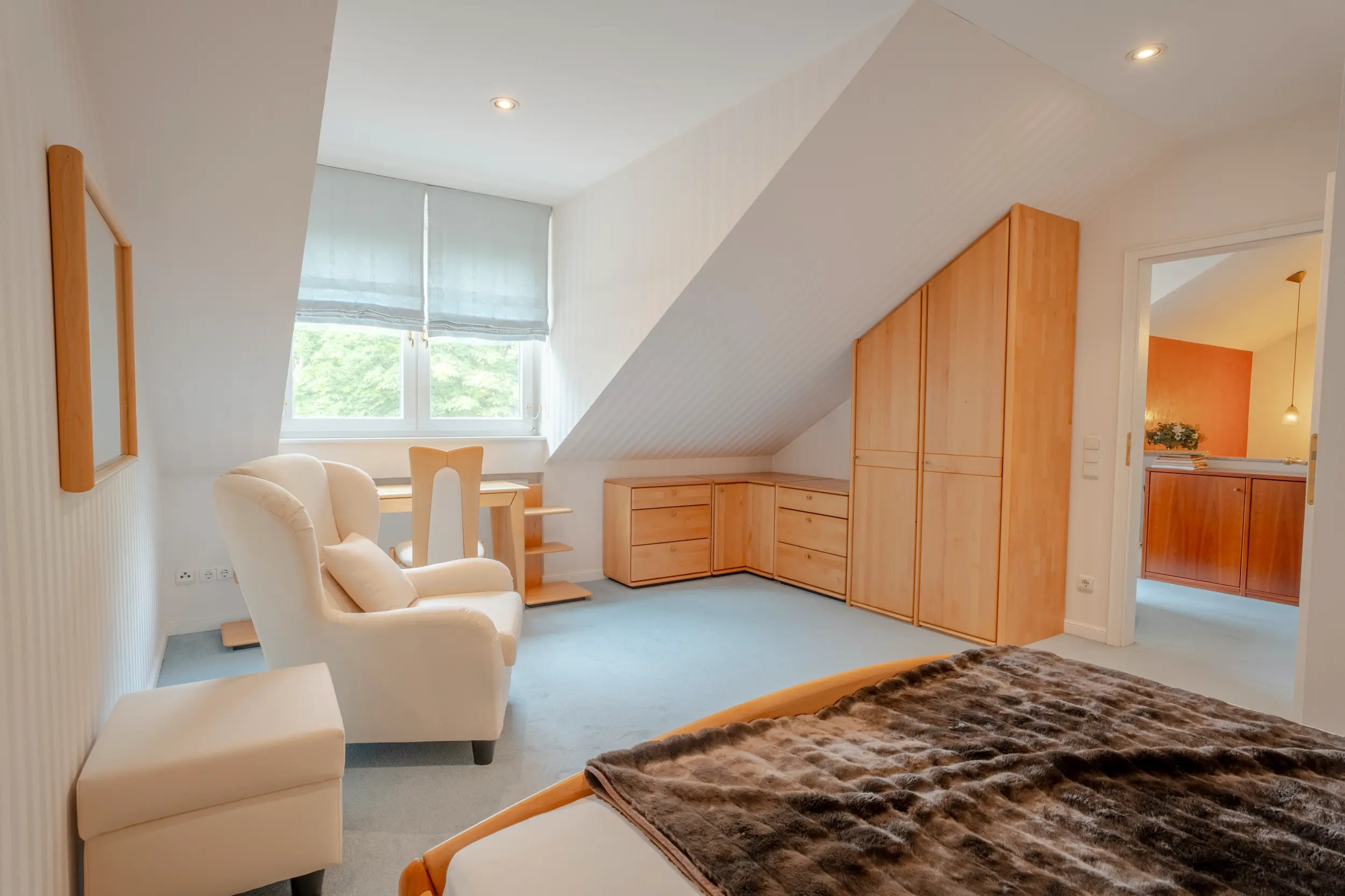 Dachgeschoss-Schlafzimmer der Villa Gronau mit hochwertigen Holzmöbeln, Sessel