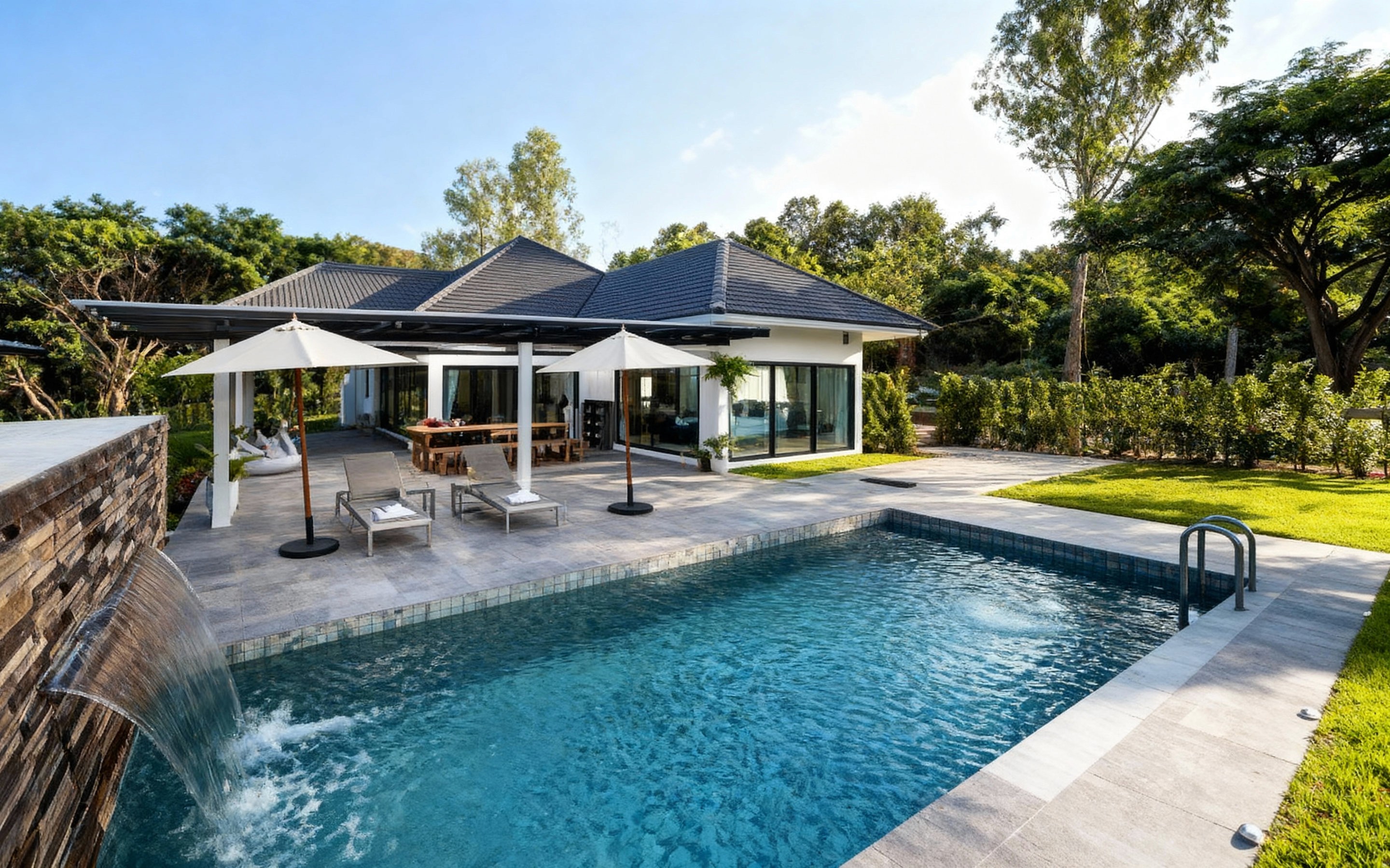 Modern white villa with a private swimming pool, waterfall feature, sun loungers, and garden views surrounded by lush greenery in Hang Dong, Chiang Mai.