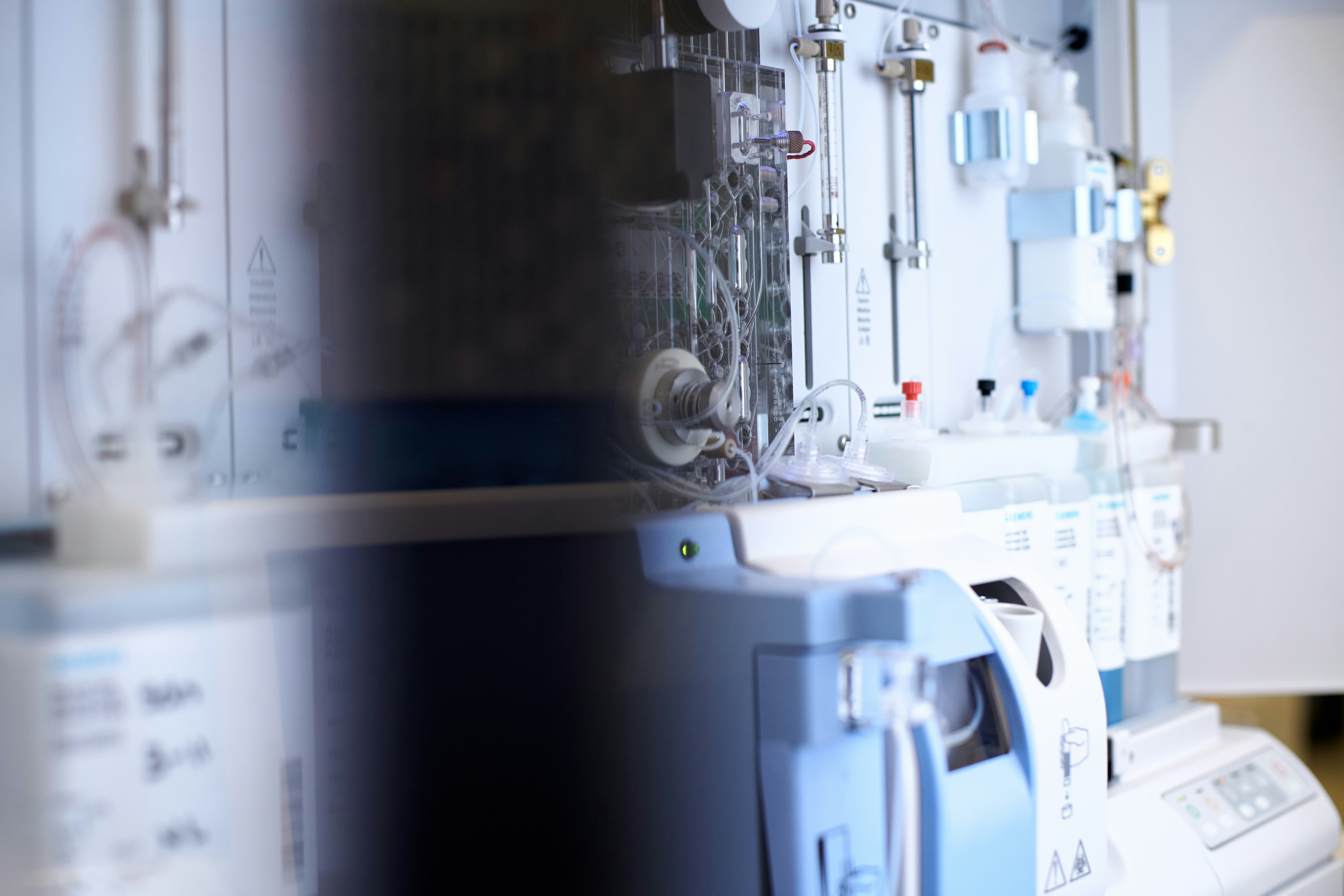 Female scientist wearing a white coat and gloves examines a sample slide in a modern laboratory setting.