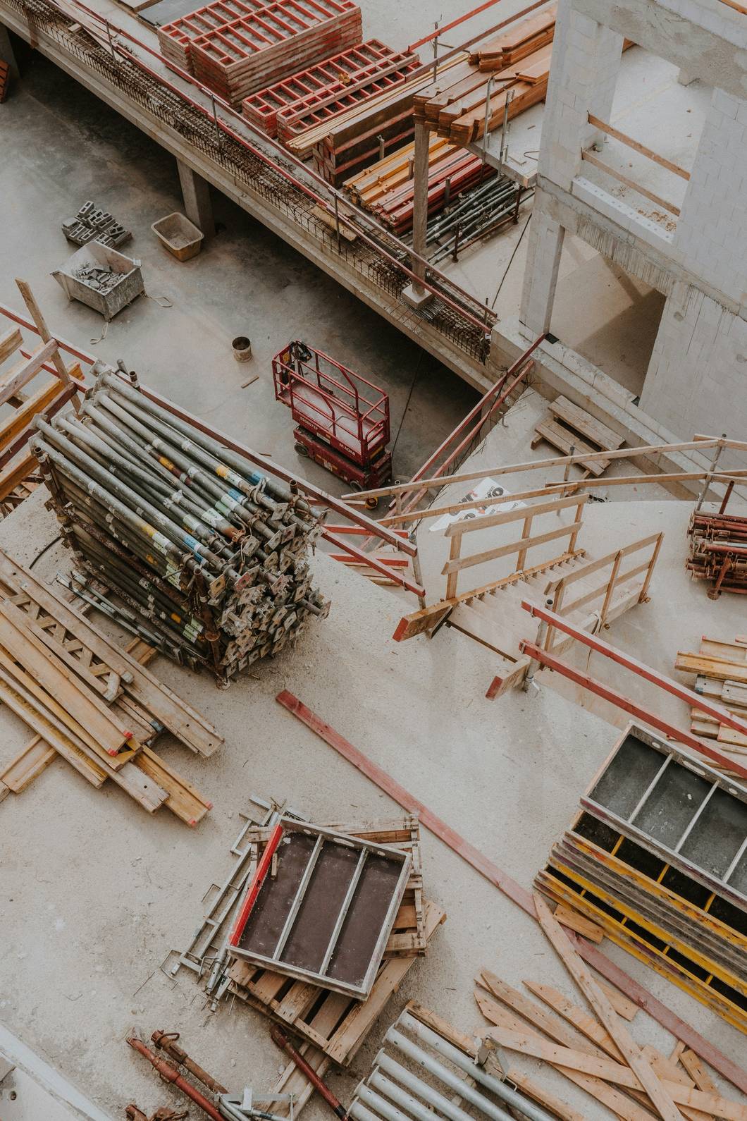 Aerial view of a construction site featuring stacked metal pipes, wooden planks, scaffolding, and building materials.