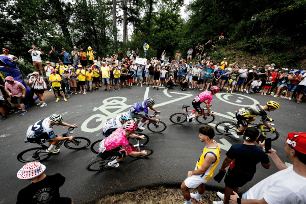Le peloton passe dans un virage bordé de spectateurs, les noms des coureurs peints sur le bitume