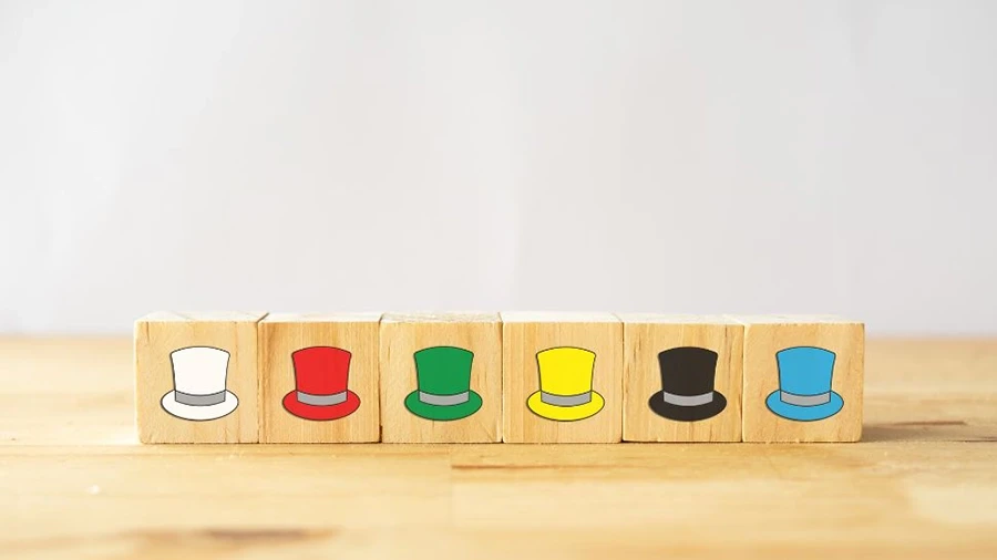 Wooden blocks displaying six colored hats representing the Six Thinking Hats concept on a wooden surface.
