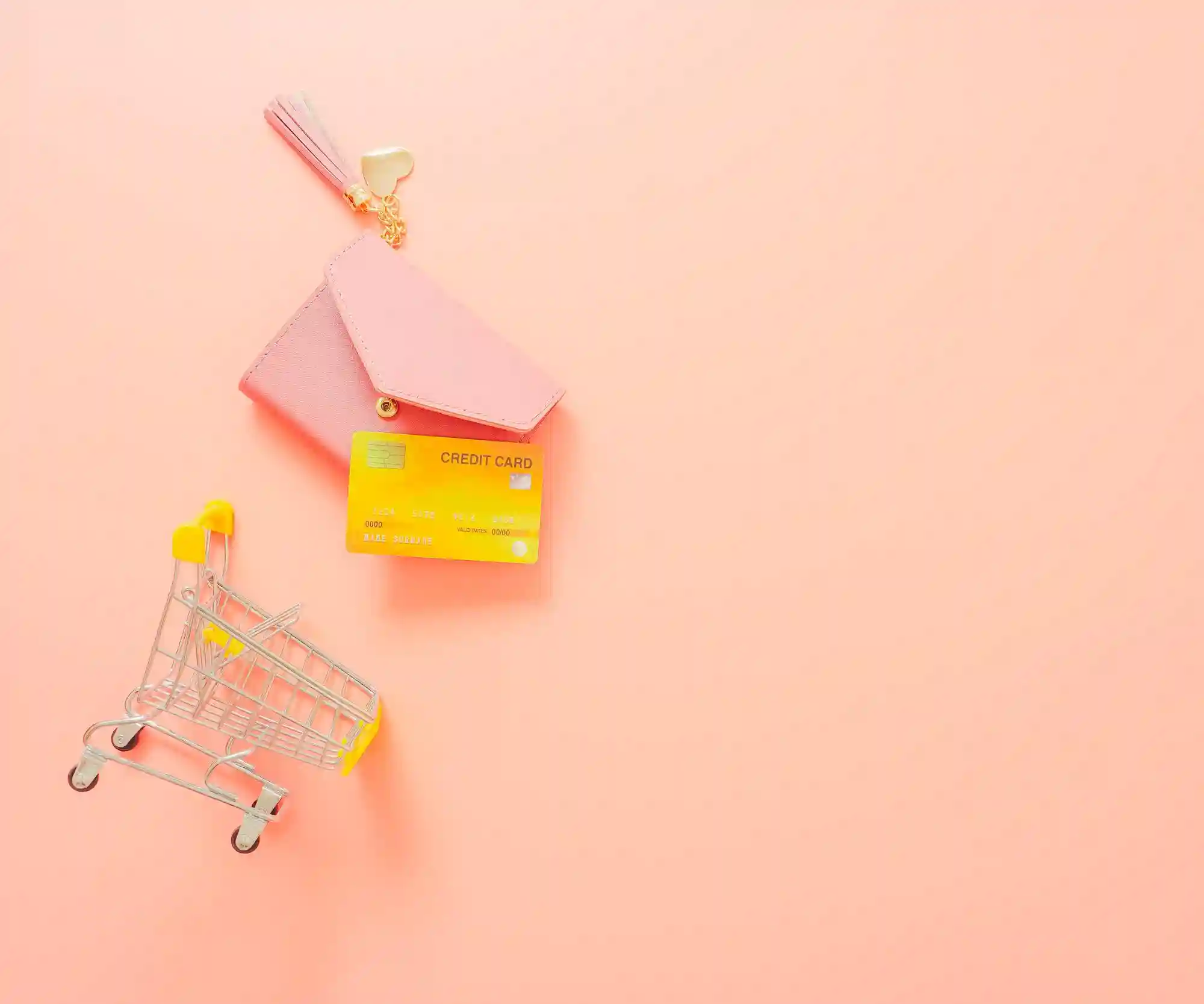 Mini shopping cart, credit card, and envelope on pink background.