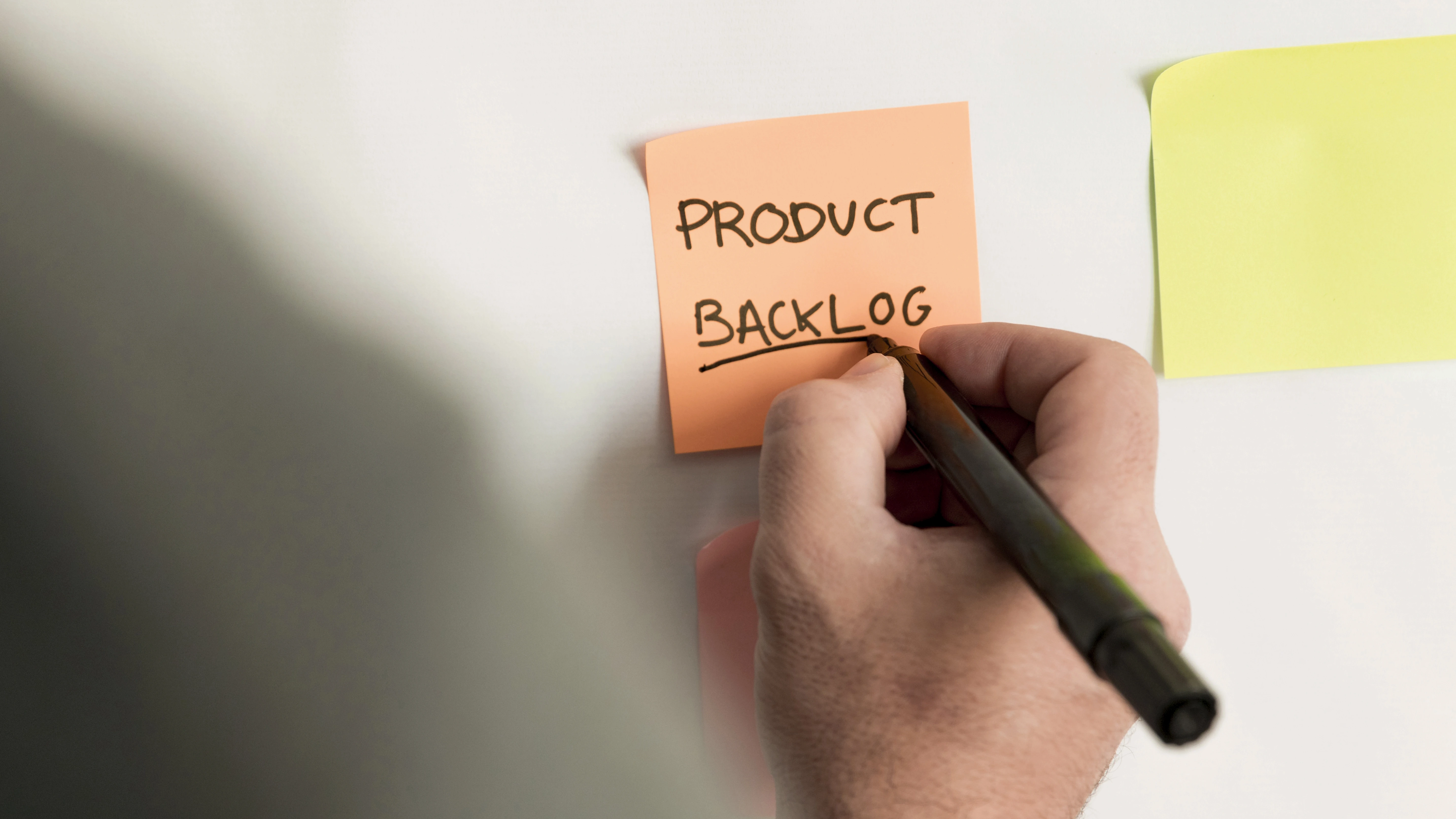Post it colado na parede com a grafia de Product Backlog, identificando a etapa de desenvolvimento de um produto digital pelo Product Owner. 