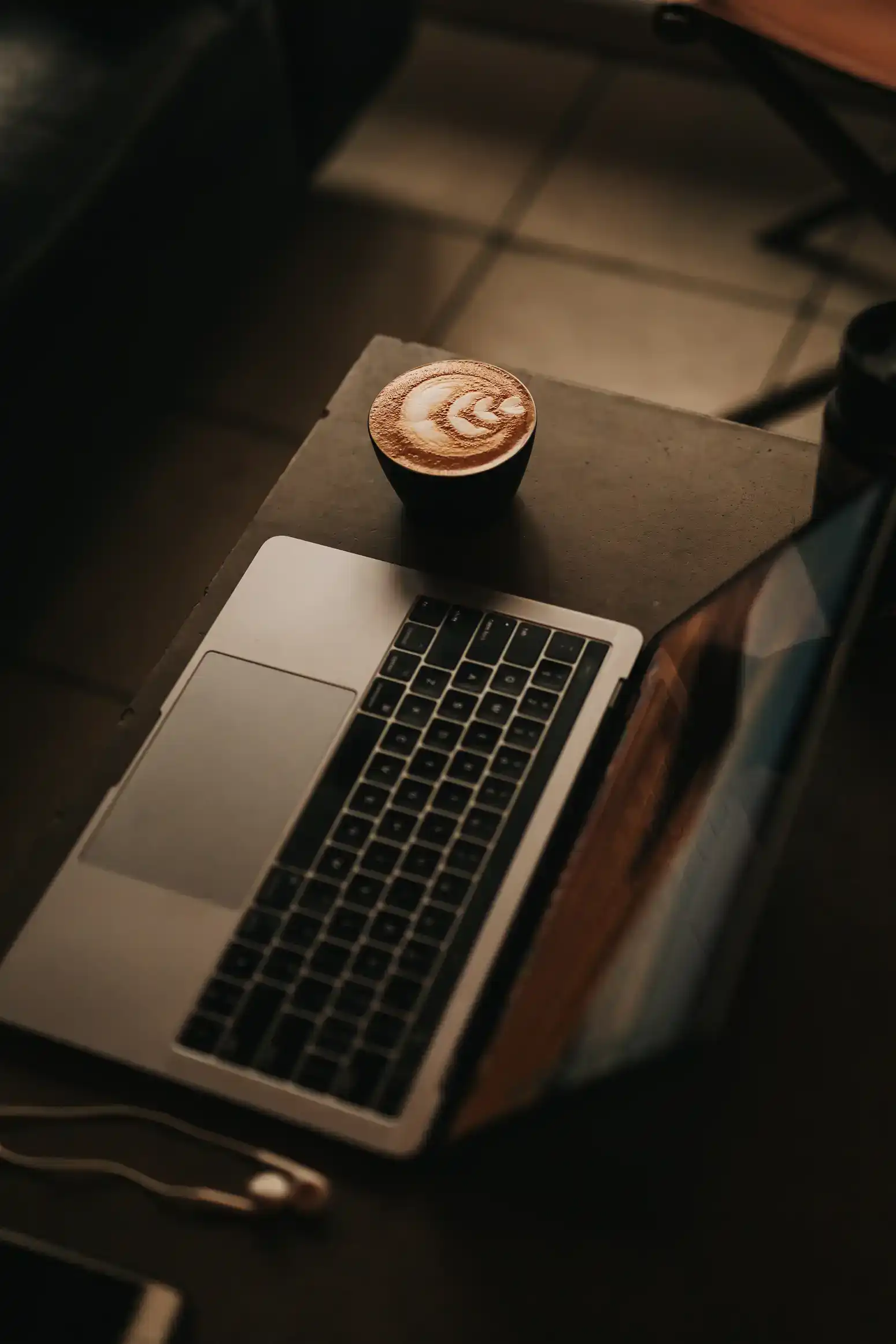 Laptop on a table next to a cup of coffee with latte art.