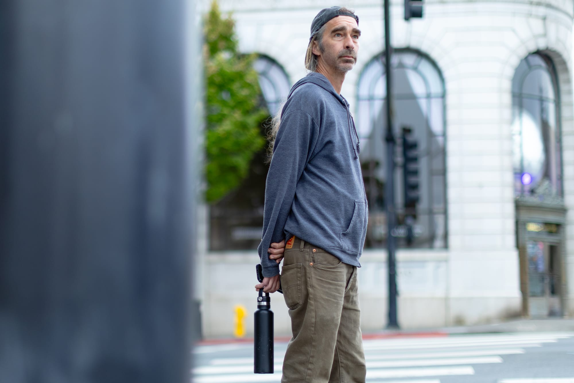 a middle-aged white in a ballcap stands in the street looking concerned holding a water bottle