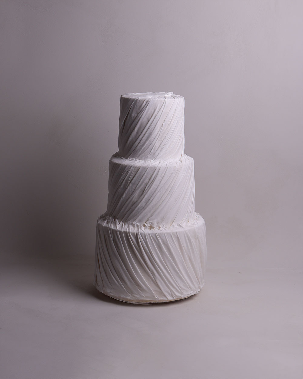 two tier white fondant wedding cake with fondant draping on front.