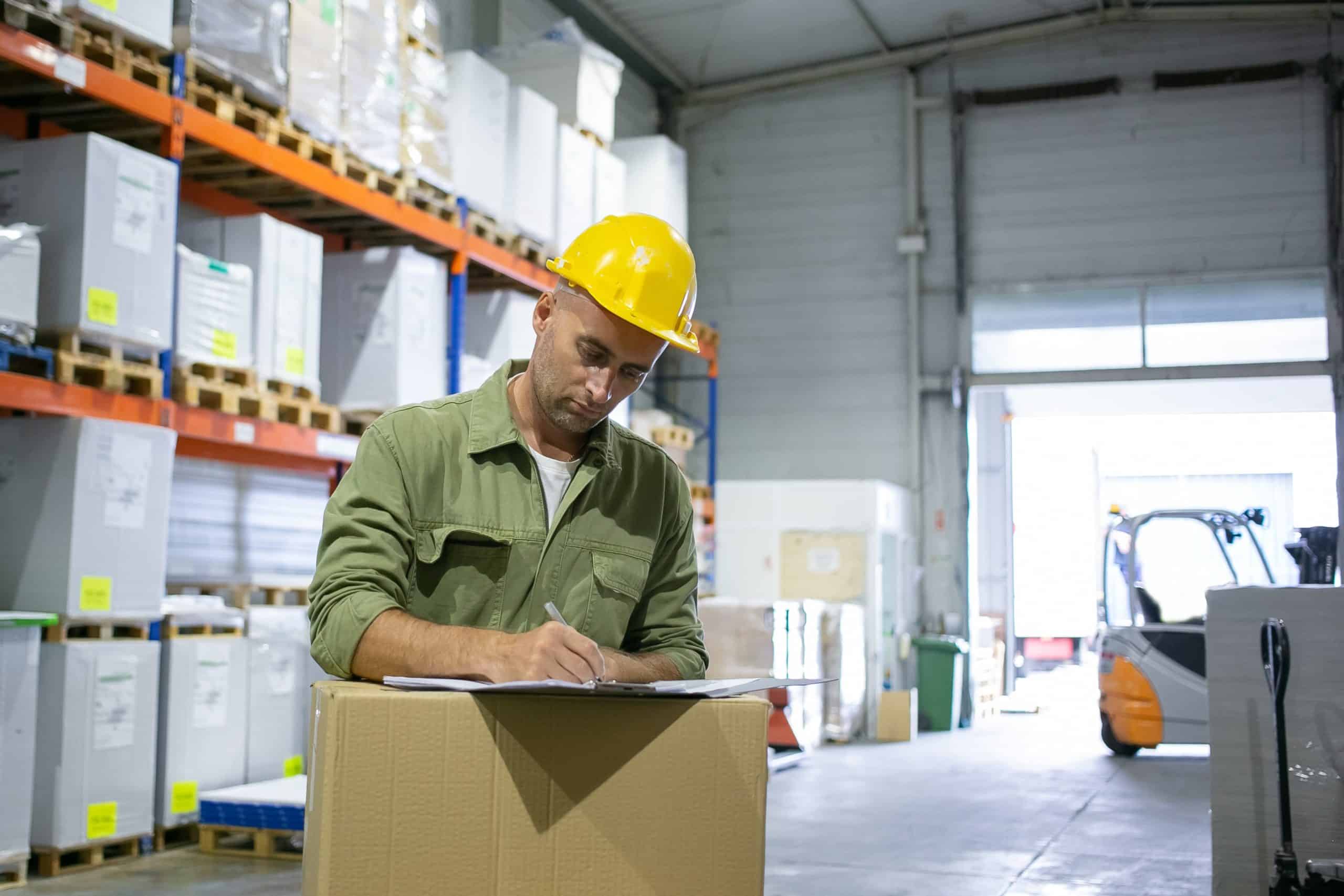 Man with safety helmet singing documents in a warehouse