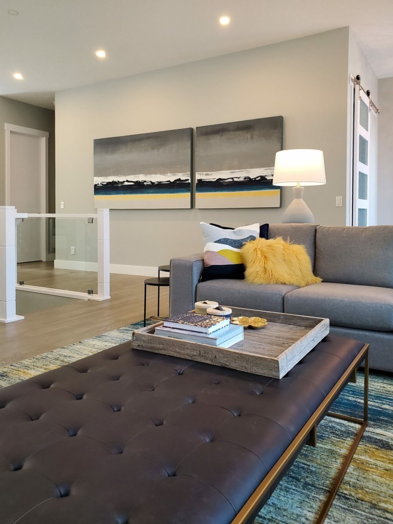 Image of Luxury living room design with gray couch, tufted ottoman, and artwork by KHD Homes designer.