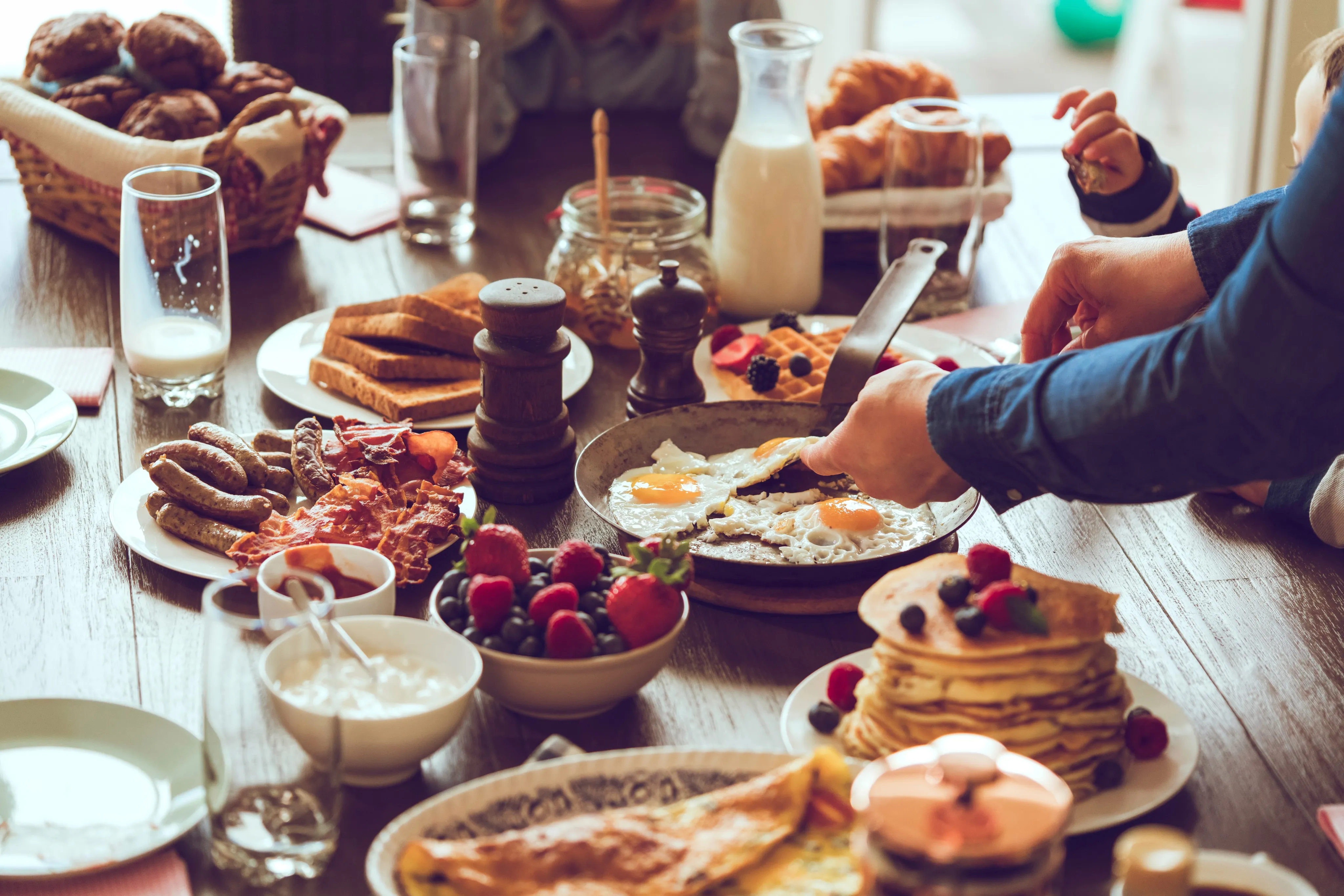 Breakfast table spread with eggs, pancakes, pastries and fresh berries