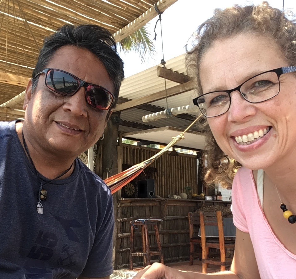 Man and woman smiling for a selfie under a bamboo-roofed outdoor patio.