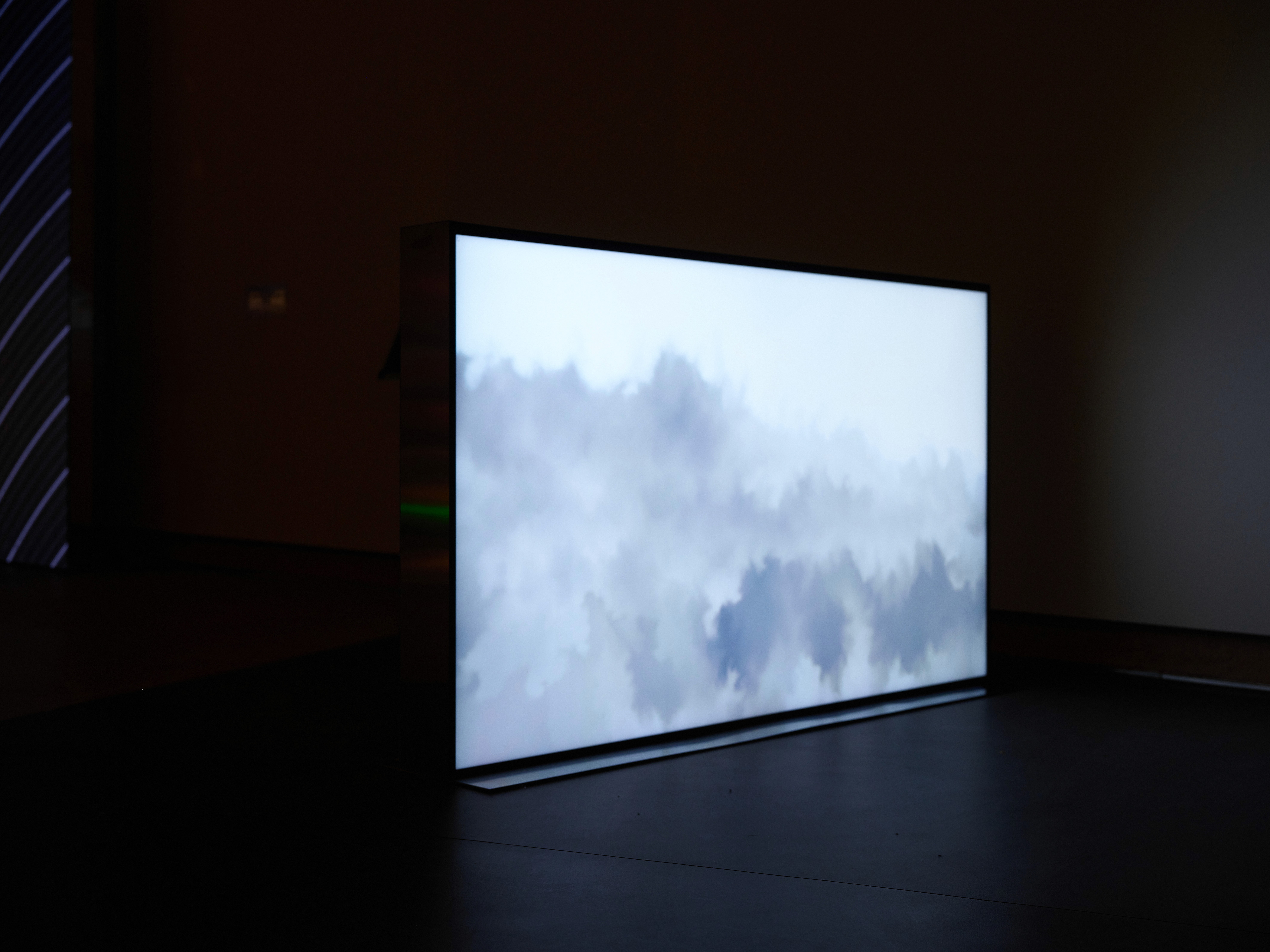Television displaying abstract cloudy sky, in dim lighting.