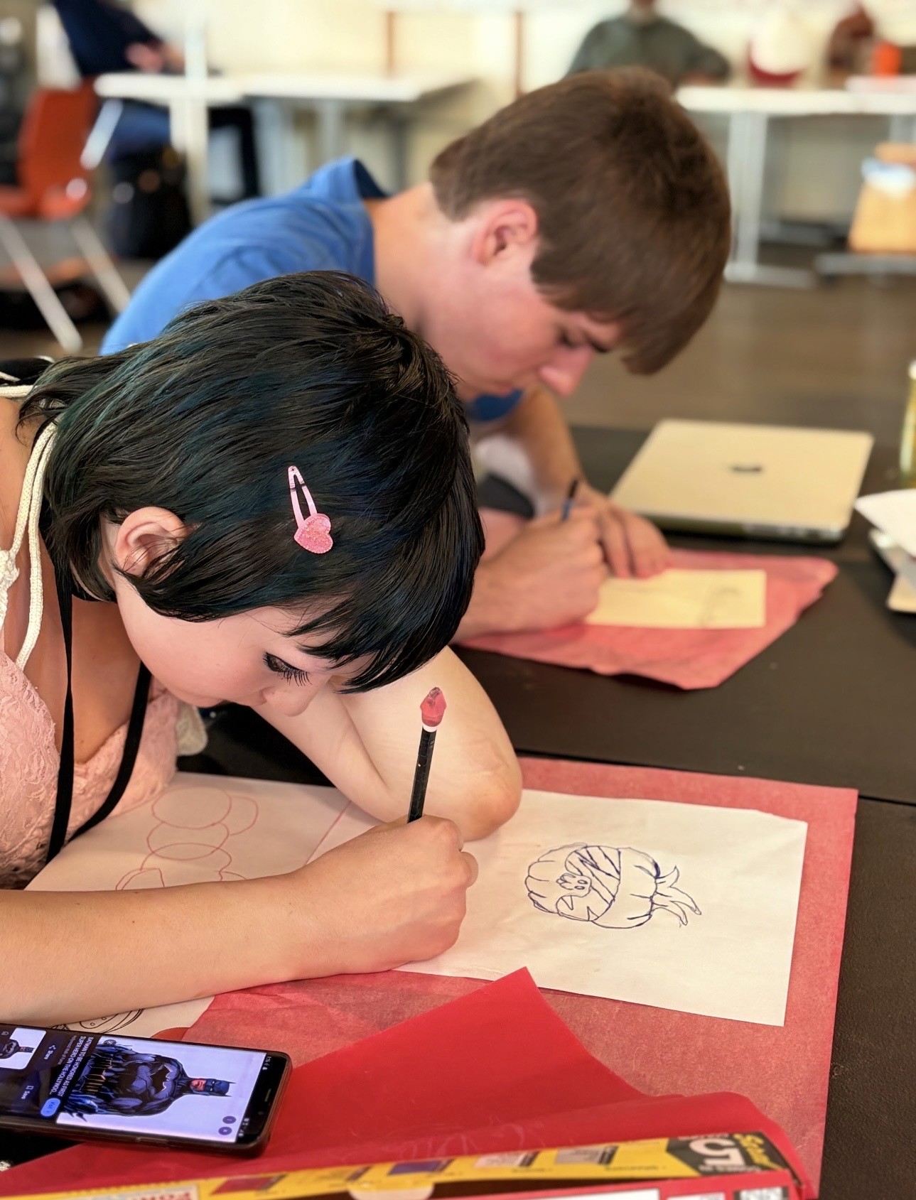 Two ArtWorks Summer Internship Program participants concentrate on creating drawings during a studio session at Access Gallery, using pencils and reference images as they develop original artwork.