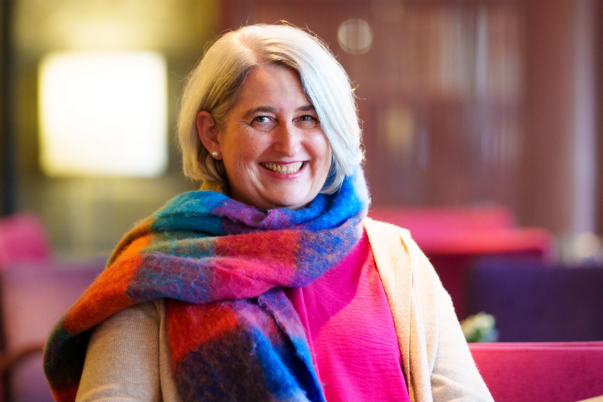 A woman sits cross-legged with eyes closed, wearing a white blouse and a long purple skirt, looking serene.