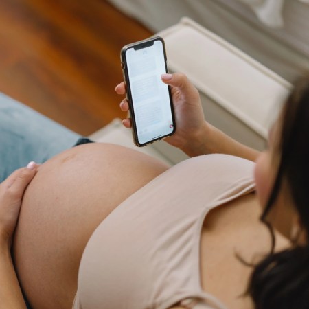 Pregnant woman relaxing on sofa while using smartphone to read or browse