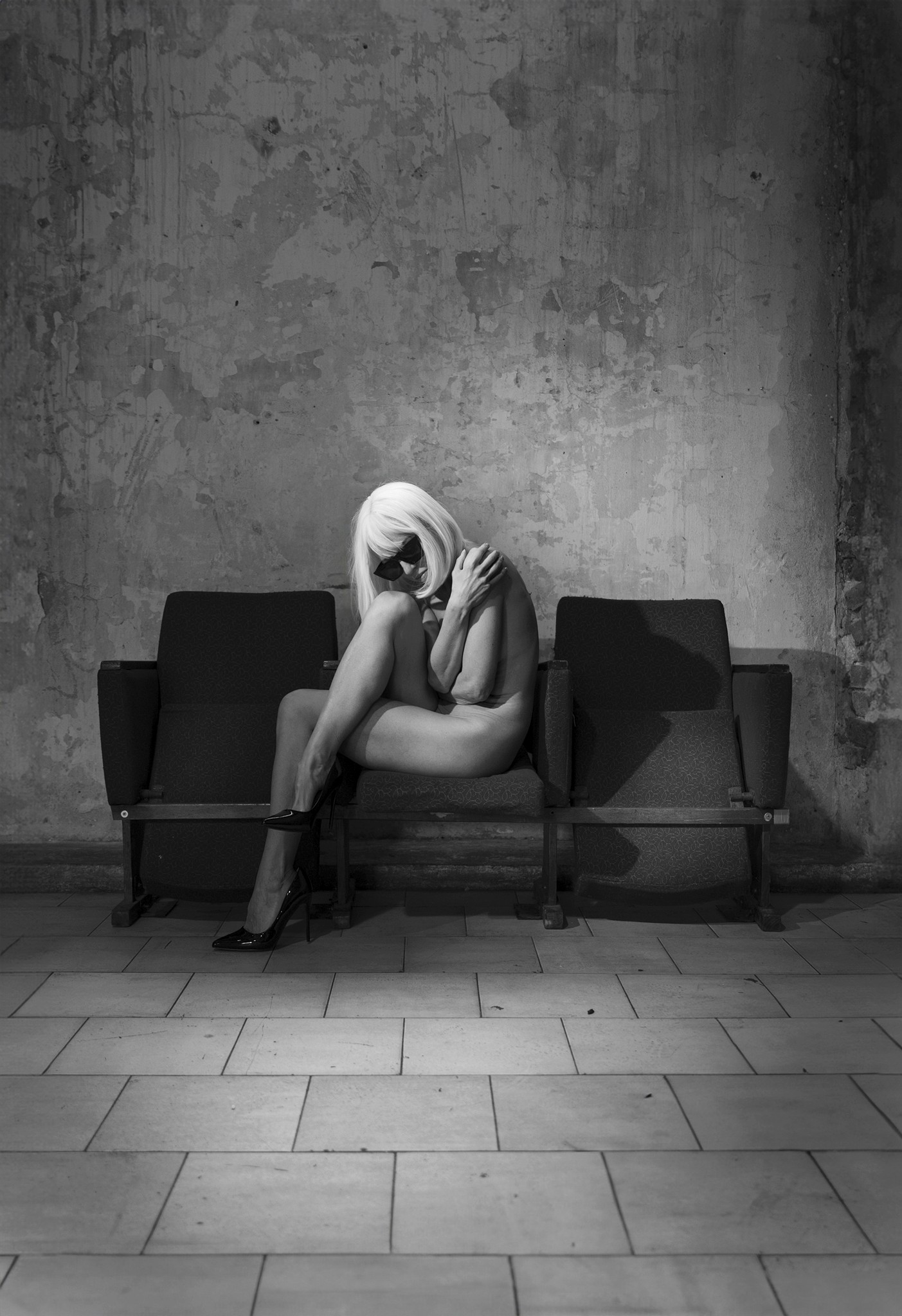 Woman in white wig curled on chair, withdrawn posture, intimate black and white fine art — Seen Not Known, Agnieszka Czyzkowska
