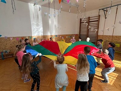 Děti hrající pohybovou hru s velkým barevným padákem