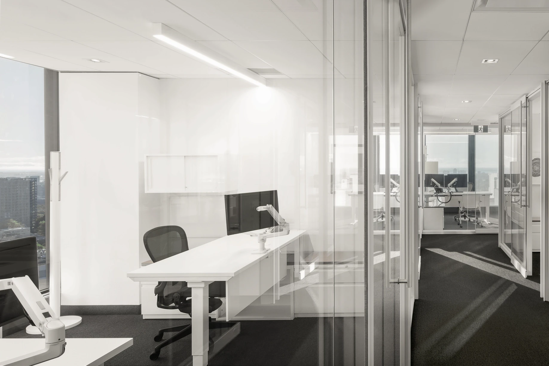 Private office enclosed by glass walls, showcasing a minimalist white desk and ergonomic chair