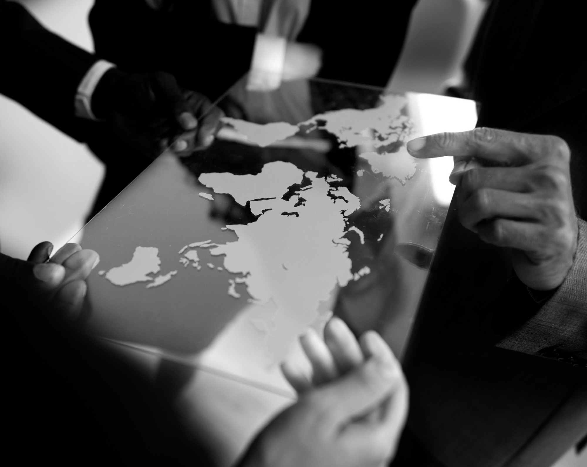 Hands pointing at a world map on a tablet during a global strategy discussion.