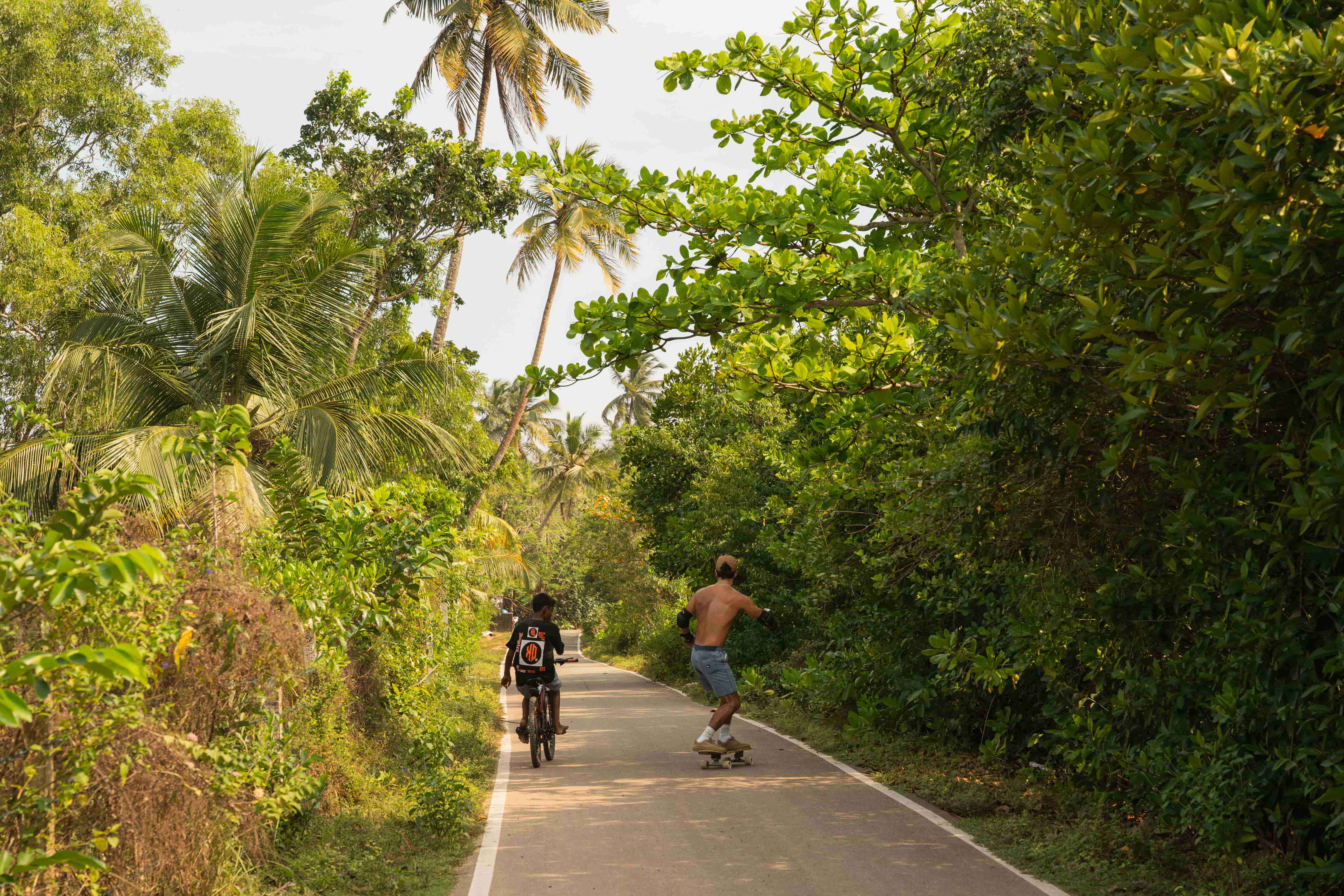 A skater and a boy on a bike on an empty street in the jungle