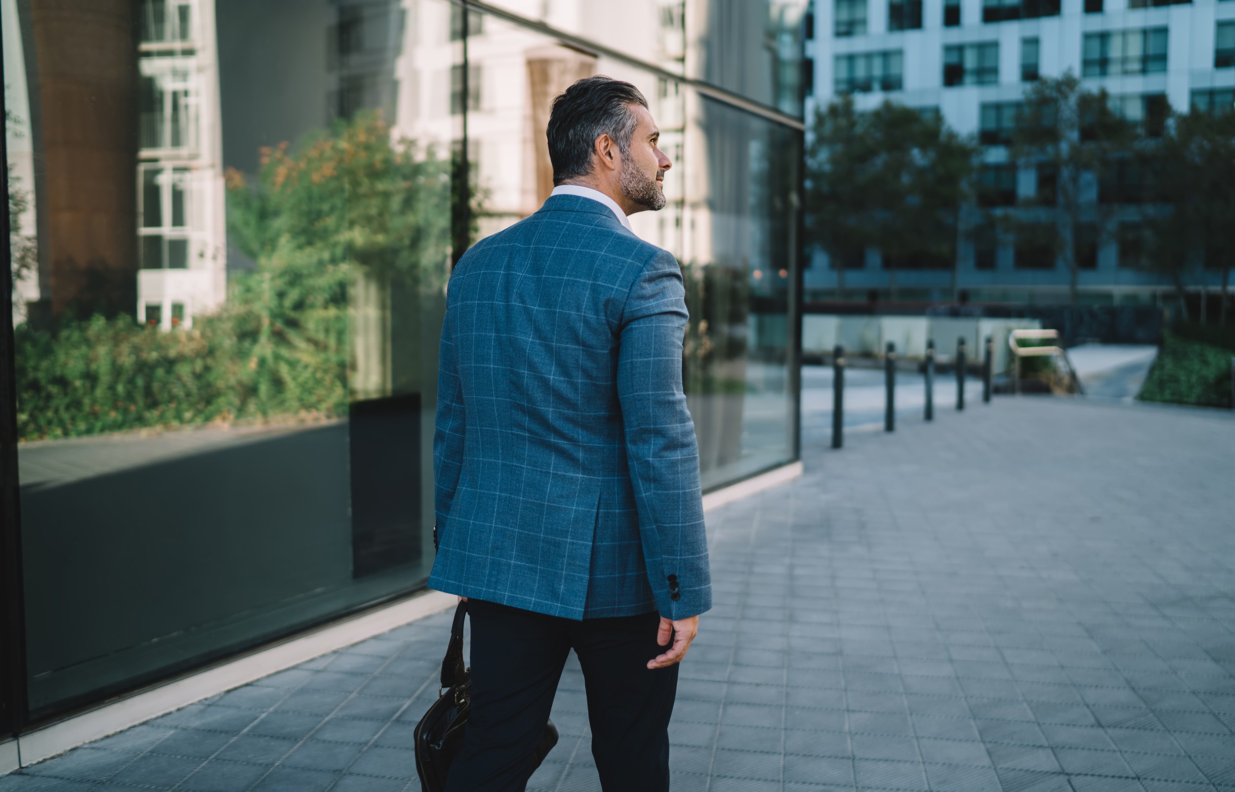 Trendy dressed proud CEO with briefcase walking at urban street and thoughtful looking away, mature Caucasian corporate director in brand clothing thinking about business deal in financial district