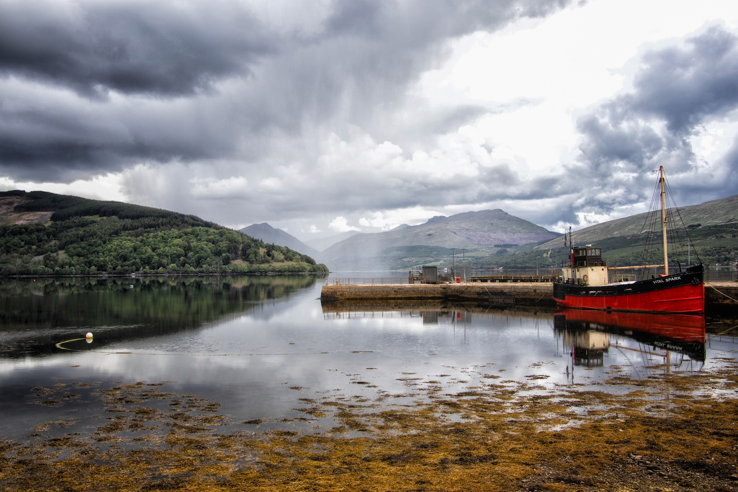 Still waters reflect a red boat and cloudy highland hills in a remote harbor inlet