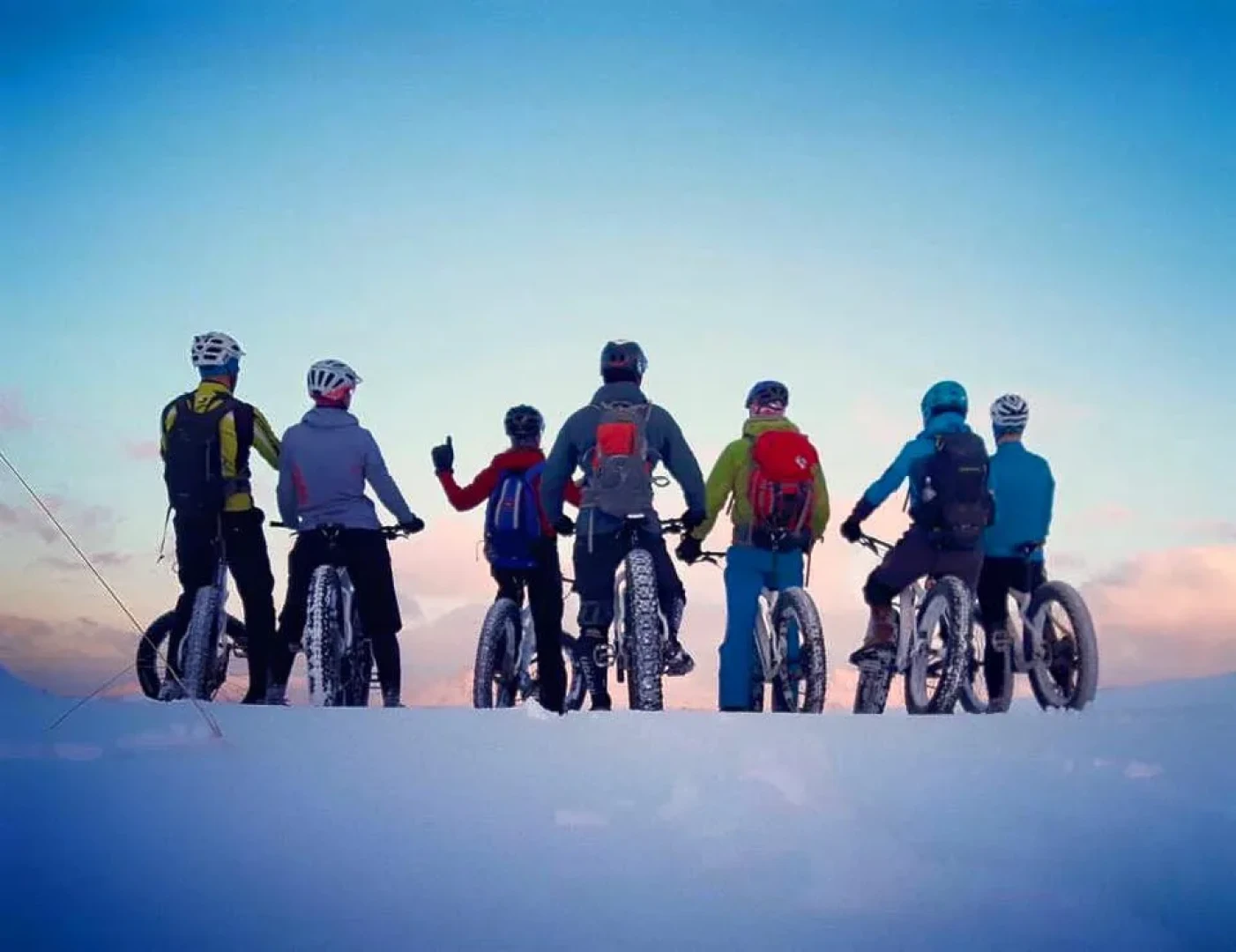 Seven fatbike riders look away from camera on a snowfield on a biketour
