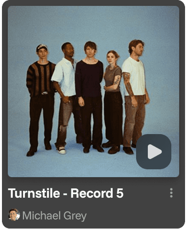 A smiling young man with crossed arms, wearing a plaid shirt and white t-shirt, poses against a dark background.