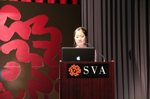 a woman giving a speech from a stand in the "designer as" thesis presentation