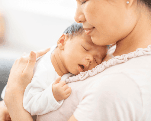 Mother holding newborn baby close to chest while baby sleeps peacefully