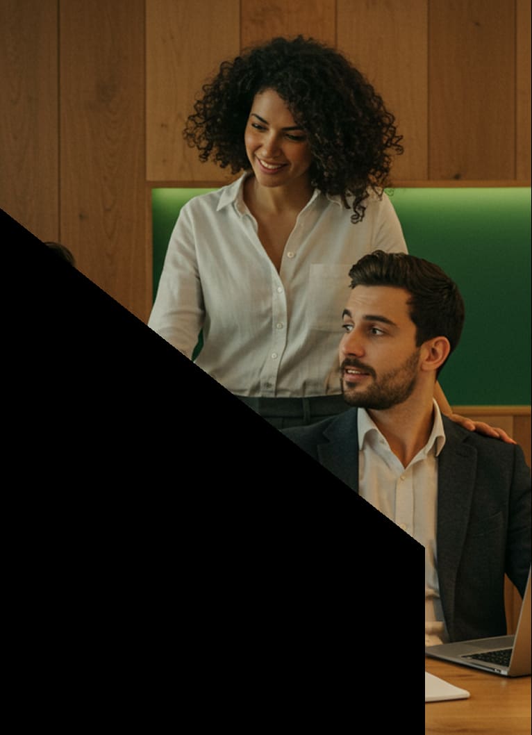 Two business professionals collaborating in a modern office setting, smiling while discussing work on a laptop.