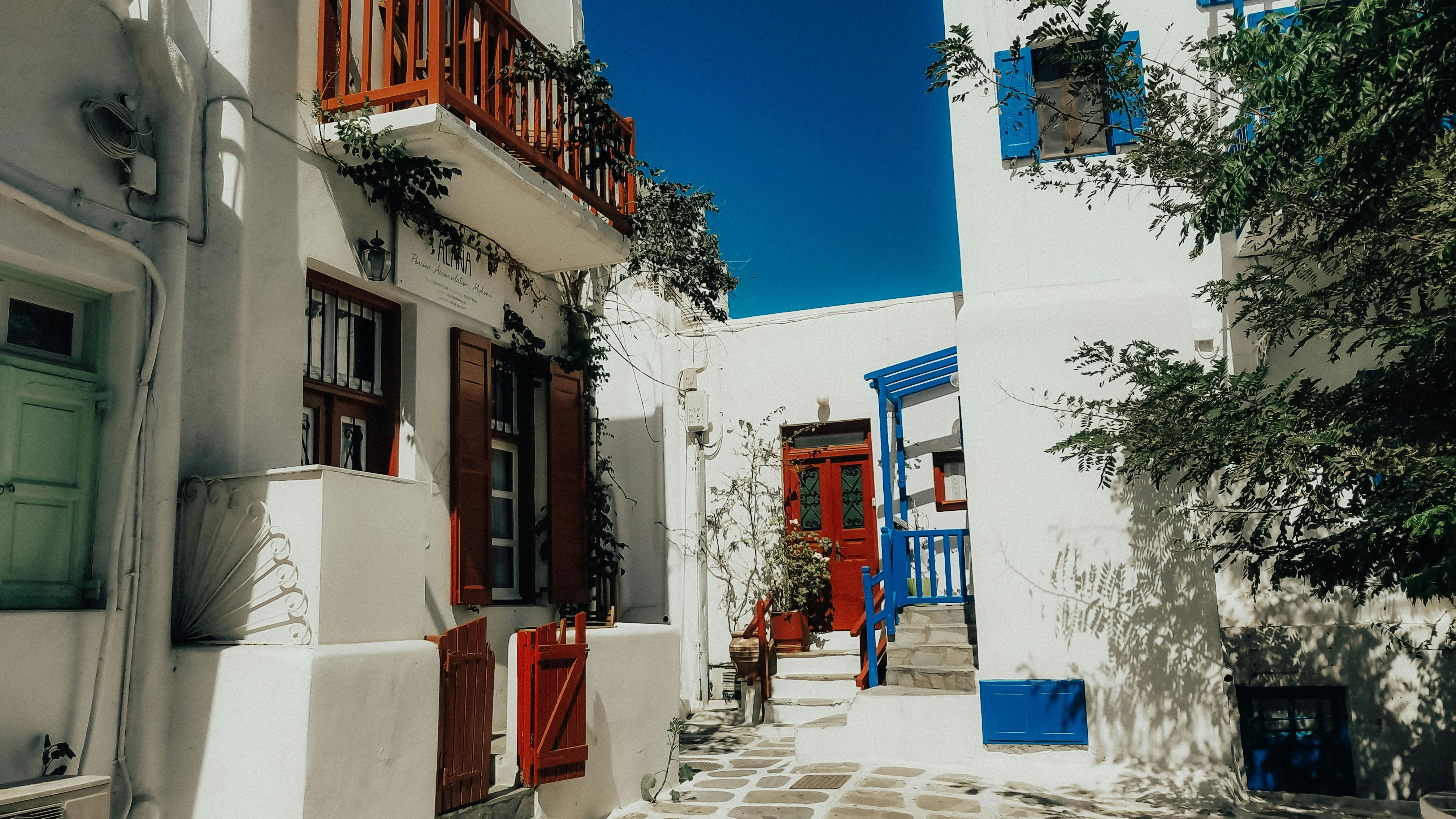 A traditional whitewashed alleyway in Mykonos with bright red and blue wooden accents.