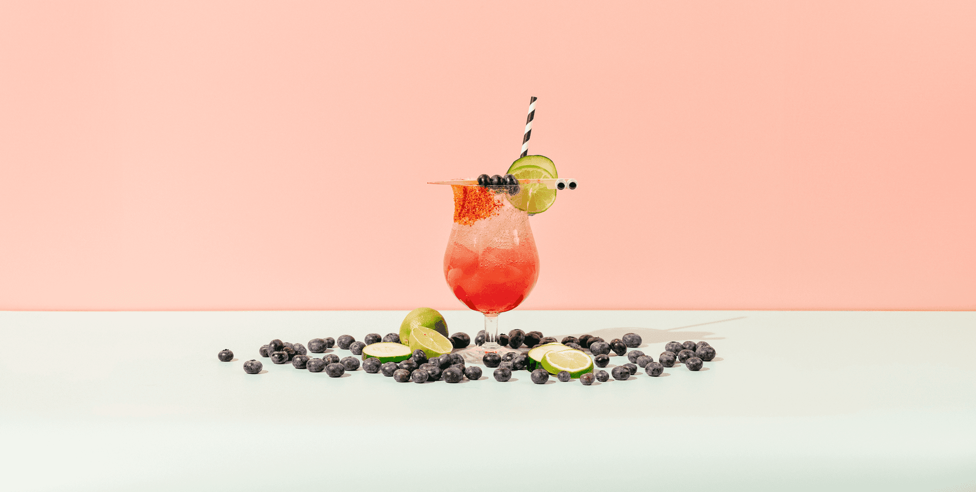 Commercial photography of a vibrant, fruity drink surrounded by blueberries on a pink background