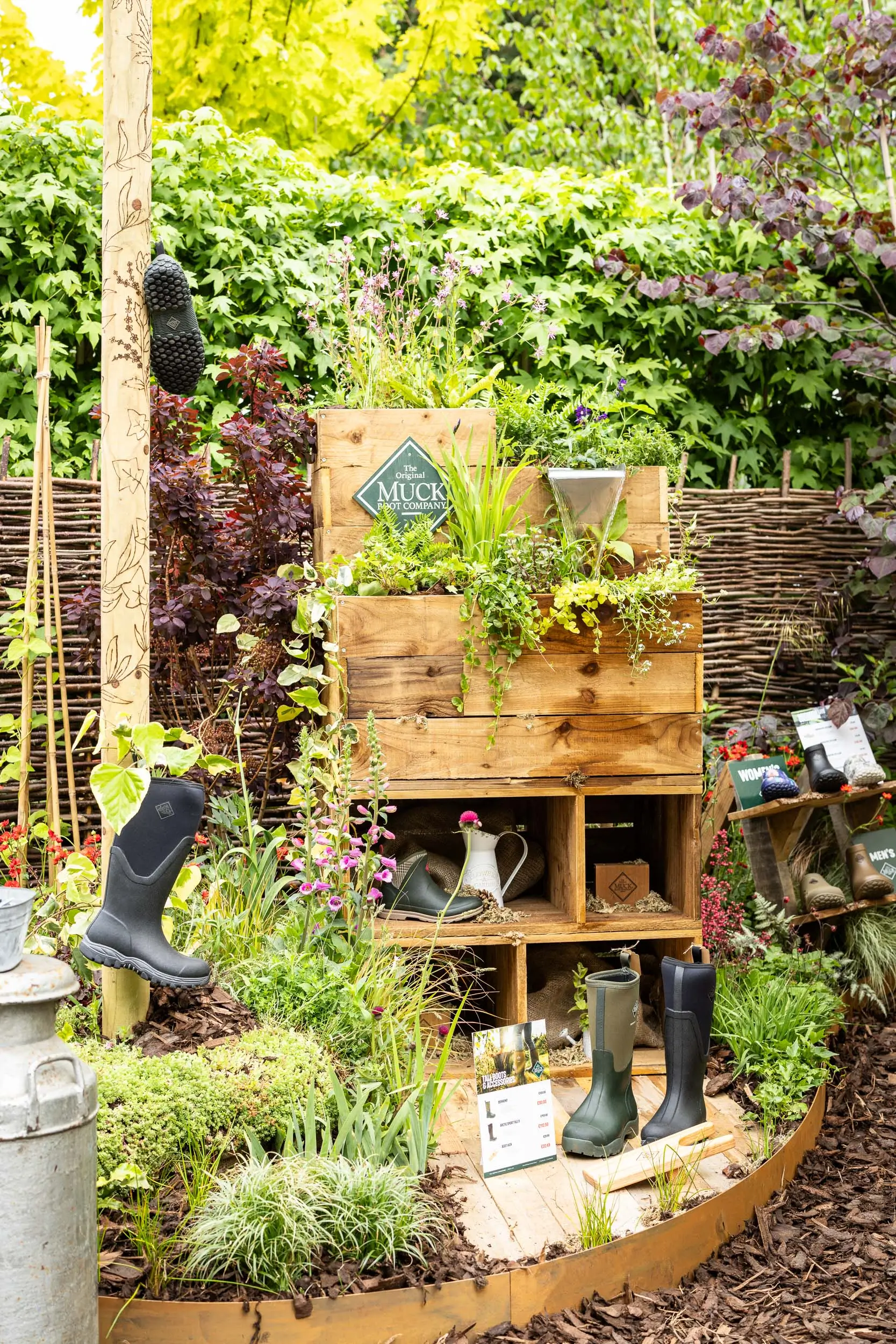 A lush garden featuring green foliage, wooden shelves, and decorative items amongst vibrant plants.