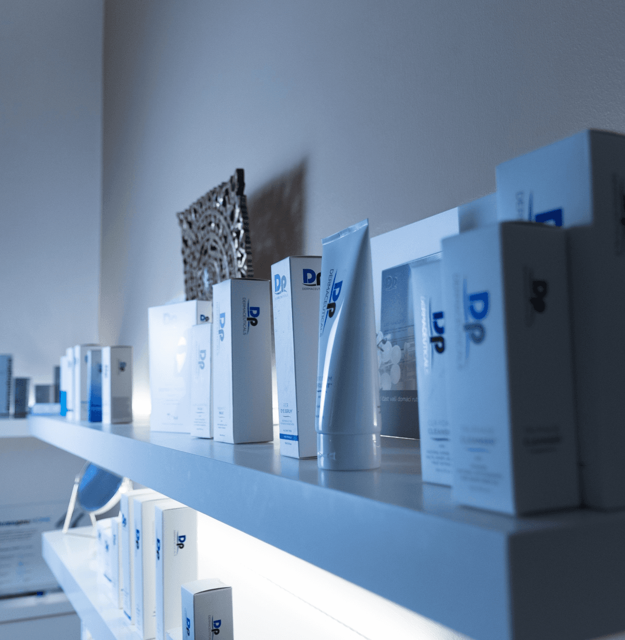 Profesionální kosmetické produkty Dermapen vystavené na bílé nástěnné polici v salonu