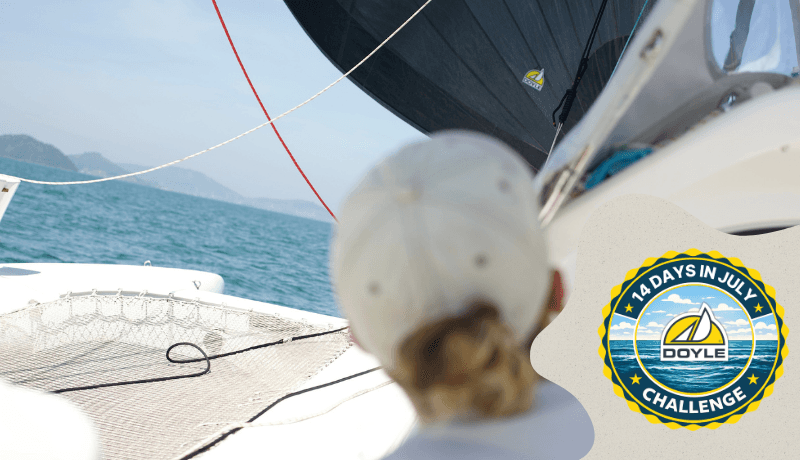 Over-the-shoulder view of a sailor aboard a catamaran sailing with a Doyle mainsail across calm coastal waters.