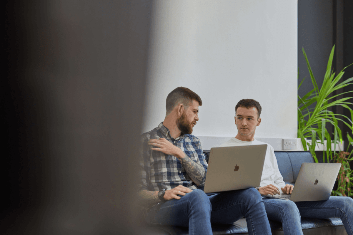 Kyle and Jason sitting on a sofa in the Komodo studio with their laptops open