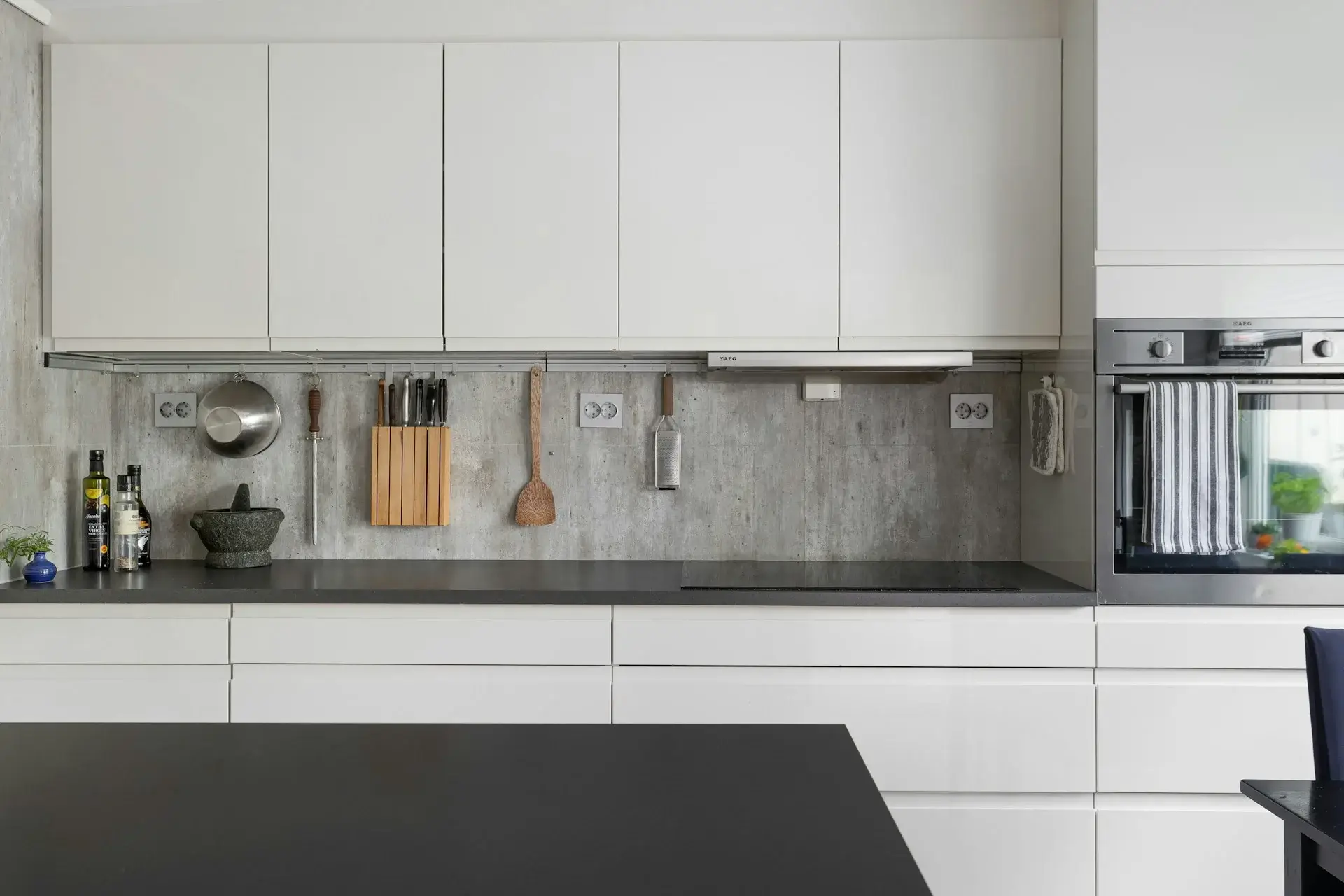 Minimal white kitchen with sleek cabinets, concrete backsplash, and black countertop.