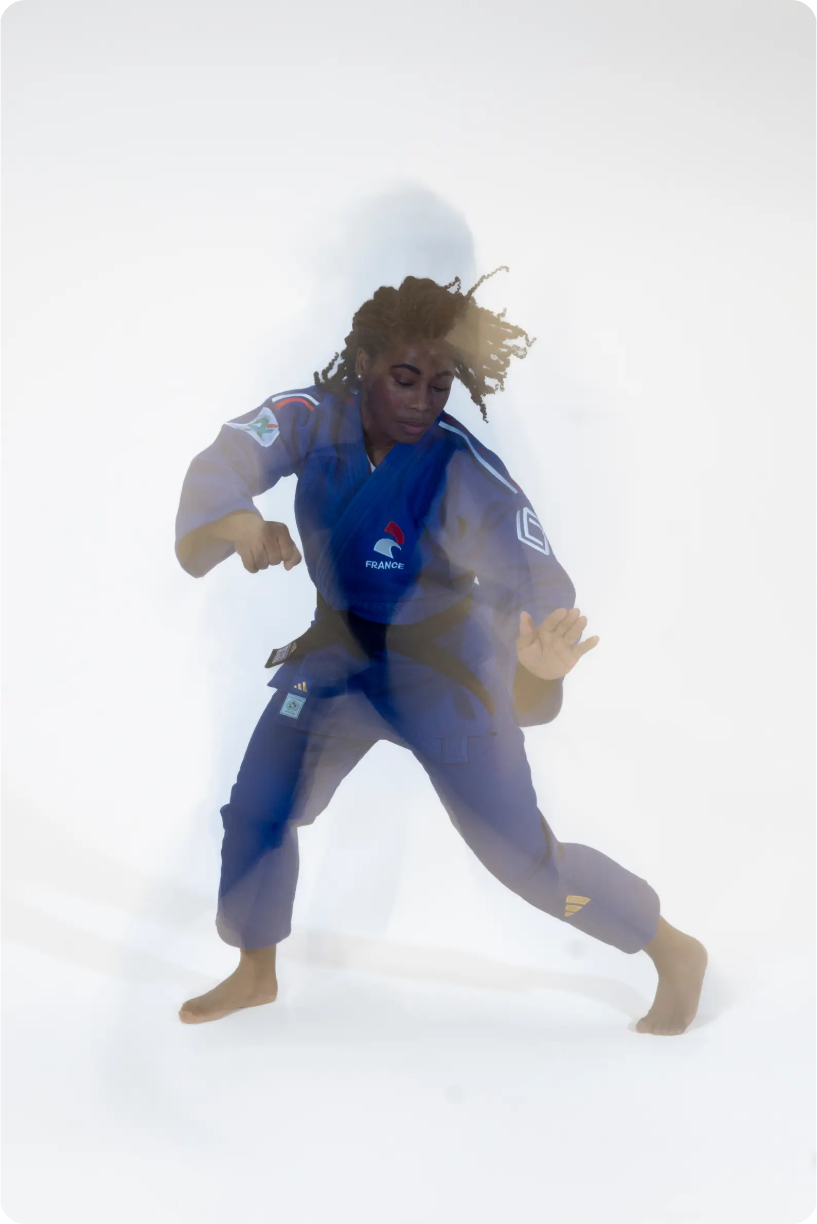 French judoka Sarah-Léonie Cysique in a blue judo uniform, photographed in studio with a motion blur effect against a white background.
