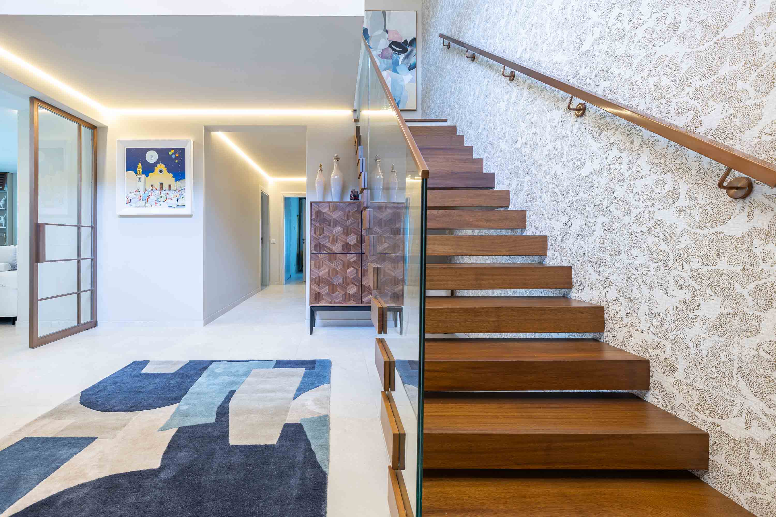 Hallway with a wooden staircase, textured wallpaper and a blue and grey rug
