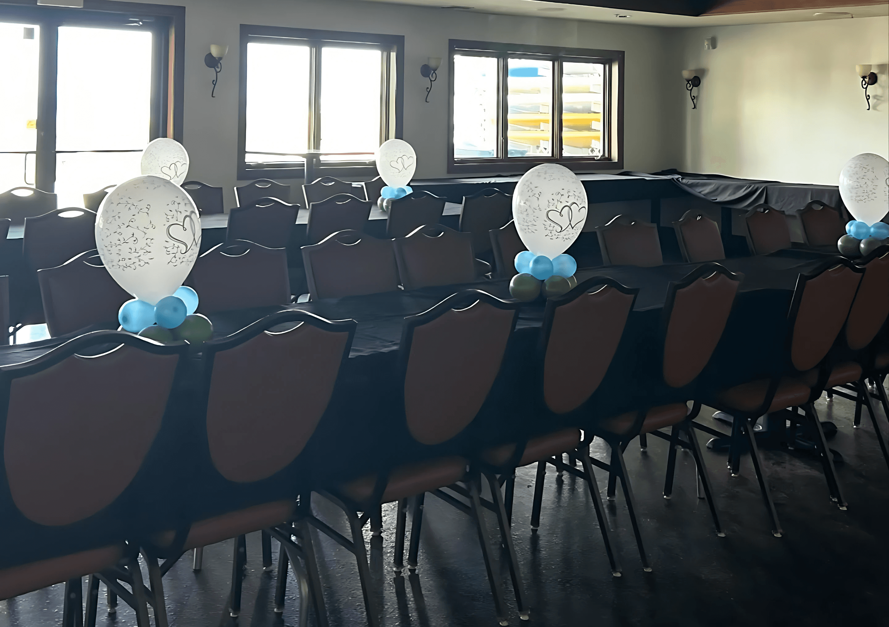 Row of chairs each decorated with blue and white balloon clusters arranged for an indoor event by Be Bold Balloons