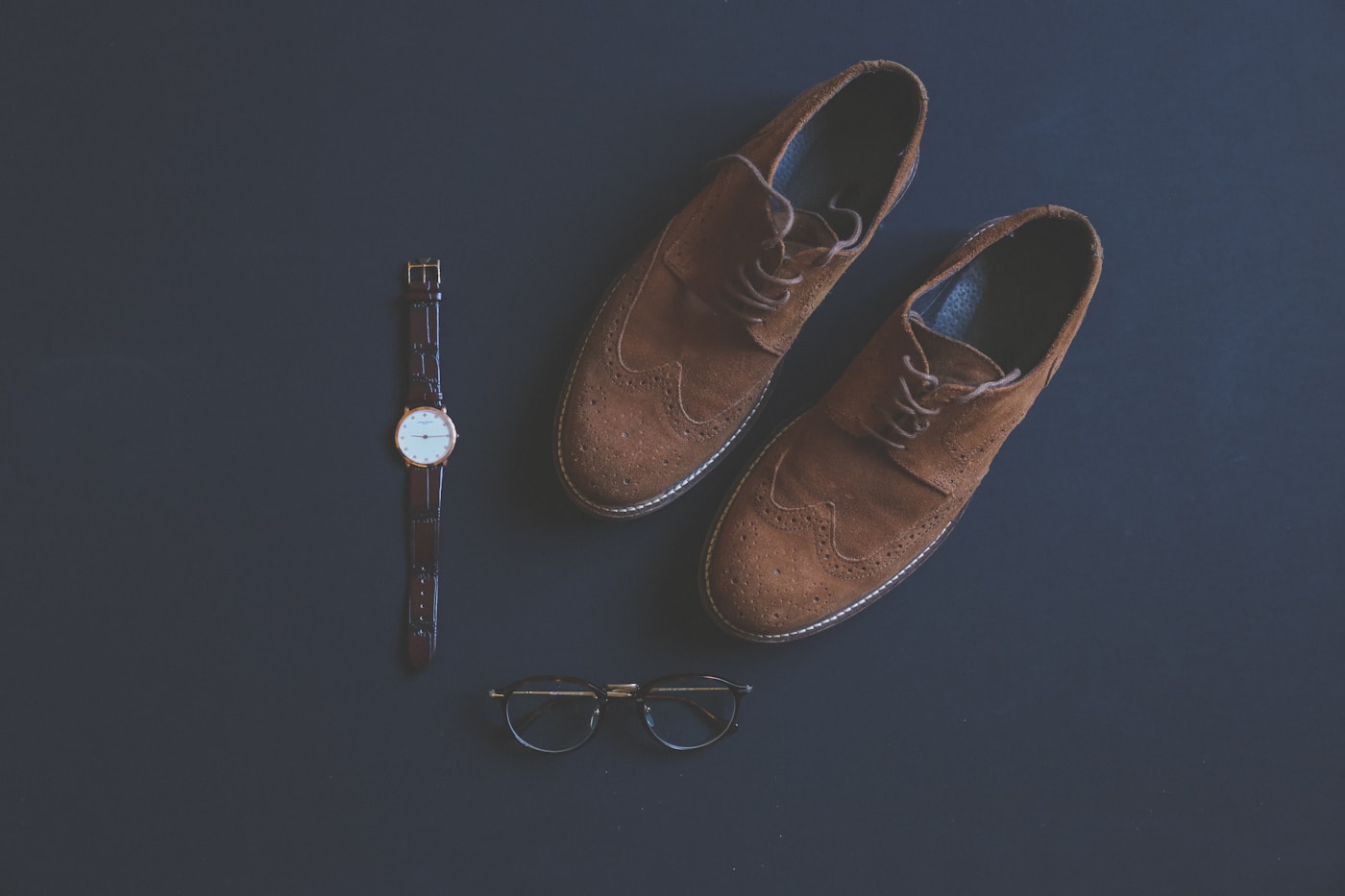 Shoes, watch, and glasses arranged as a coordinated fashion look